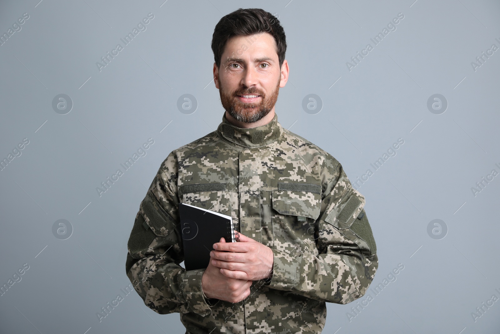 Photo of Happy soldier with notebook on light grey background. Military service