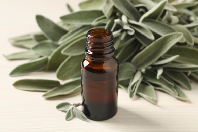 Photo of Bottle of essential sage oil and leaves on white wooden table