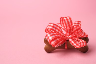 Photo of Bone shaped dog cookie with red bow on pink background, closeup. Space for text