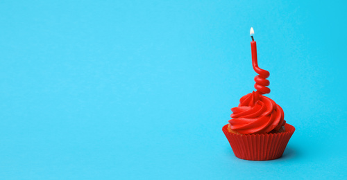 Delicious birthday cupcake with red cream and burning candle on light blue background. Space for text