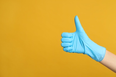 Doctor in medical gloves showing thumb up on yellow background, closeup. Space for text