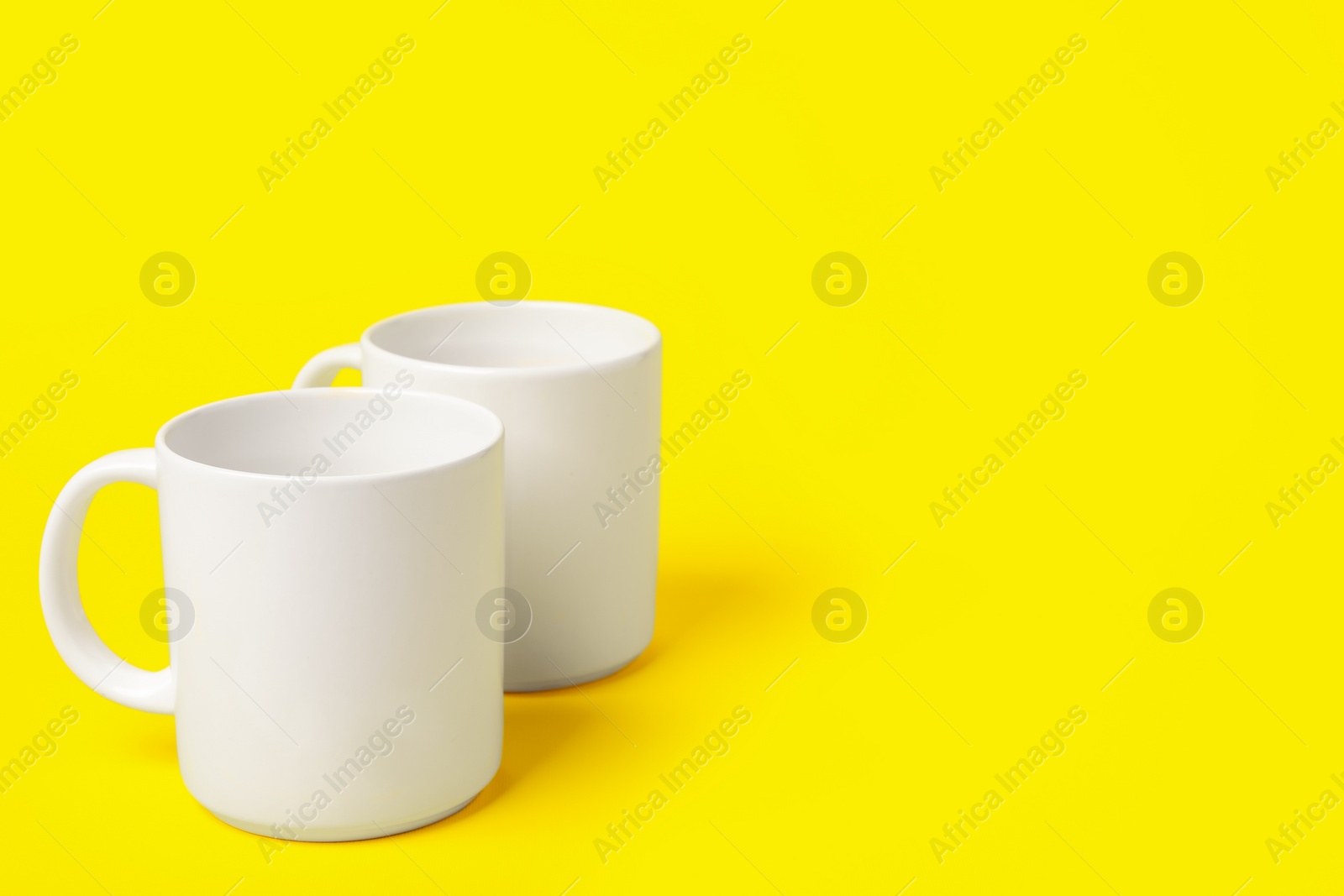 Photo of Two white ceramic mugs on yellow background, space for text