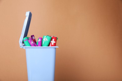 Photo of Many used batteries in recycling bin on light brown background. Space for text