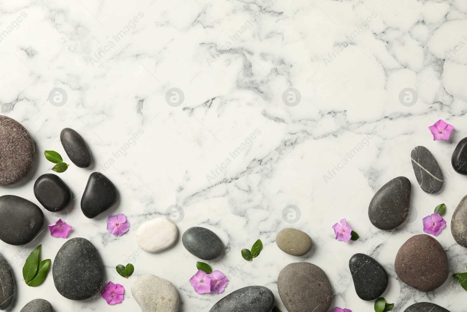 Photo of Spa stones, petunia flowers and green leaves on white marble table, flat lay. Space for text