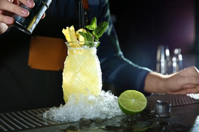 Barman making tropical cocktail at counter in pub, closeup. Space for text
