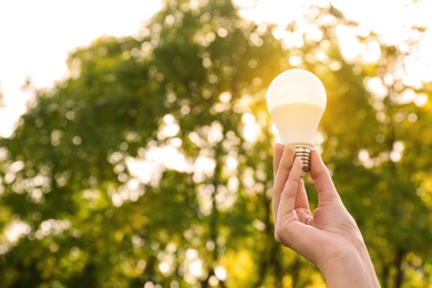 Photo of Woman holding lamp bulb outdoors, closeup. Space for text