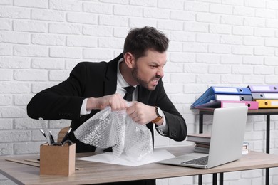 Photo of Businessman popping bubble wrap at workplace in office. Stress relief