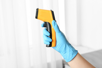 Doctor in gloves holding non contact infrared thermometer indoors, closeup