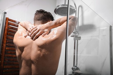 Photo of Handsome man taking shower at home, back view