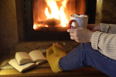 Photo of Woman with cup of hot cocoa near fireplace at home, closeup. Space for text