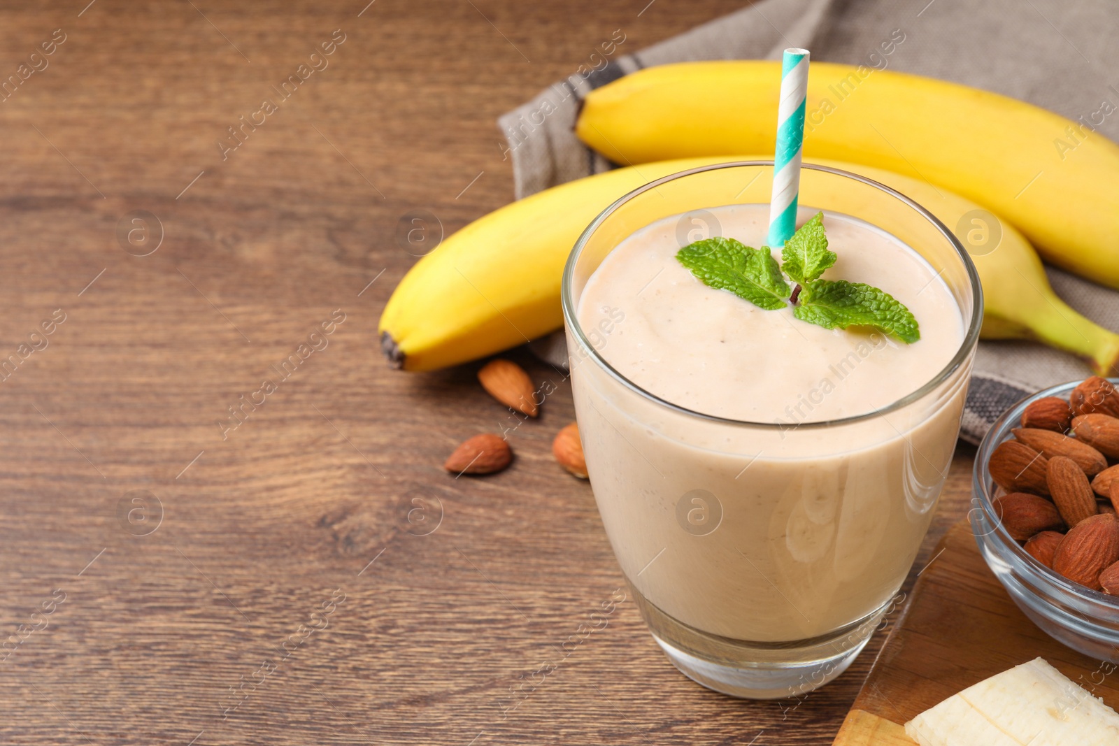 Photo of Glass with banana smoothie and mint on wooden table. Space for text