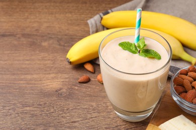 Photo of Glass with banana smoothie and mint on wooden table. Space for text