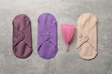 Photo of Menstrual cup and cloth pads on grey background, flat lay. Reusable feminine hygiene products