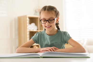 Photo of Cute little girl reading book at desk in room