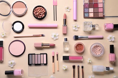 Photo of Flat lay composition with different makeup products and beautiful spring flowers on beige background