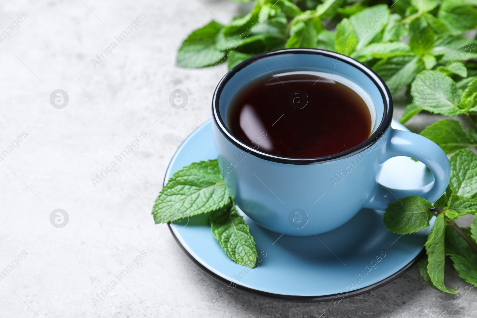 Photo of Cup with hot aromatic mint tea and fresh leaves on light grey table, closeup. Space for text