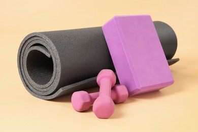 Photo of Grey exercise mat, yoga block and dumbbells on beige background