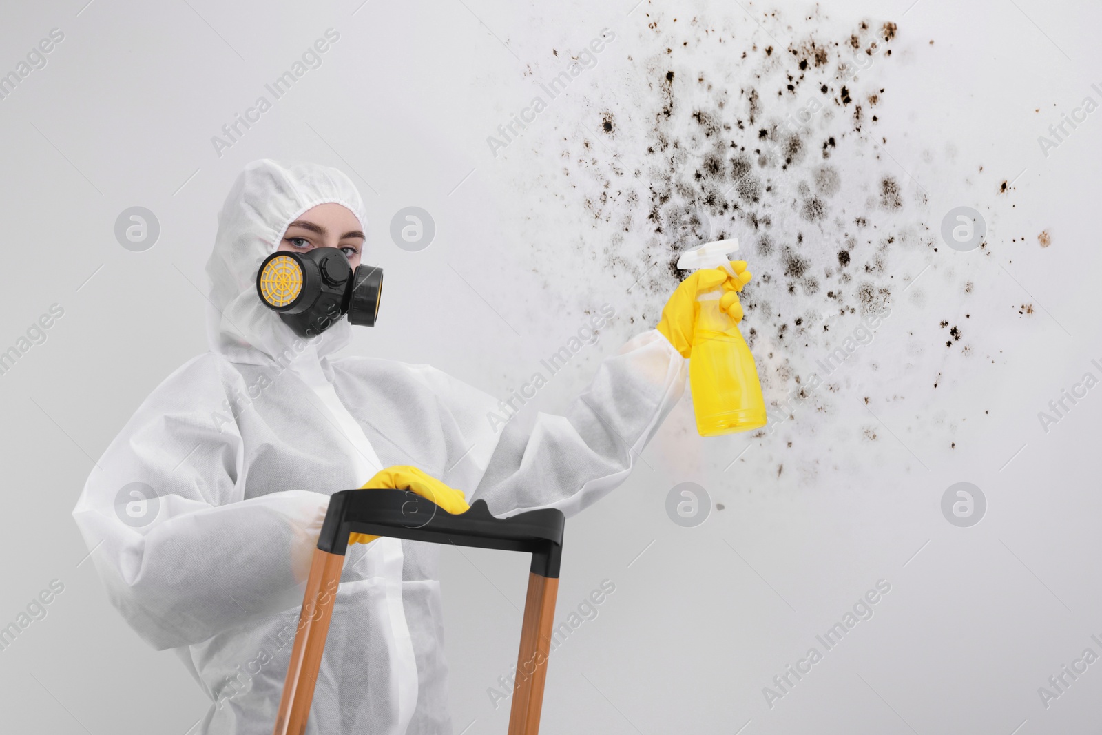 Image of Woman in protective suit and rubber gloves using mold remover on wall