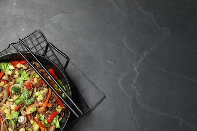 Photo of Stir fried noodles with mushrooms and vegetables in wok on black table, top view. Space for text