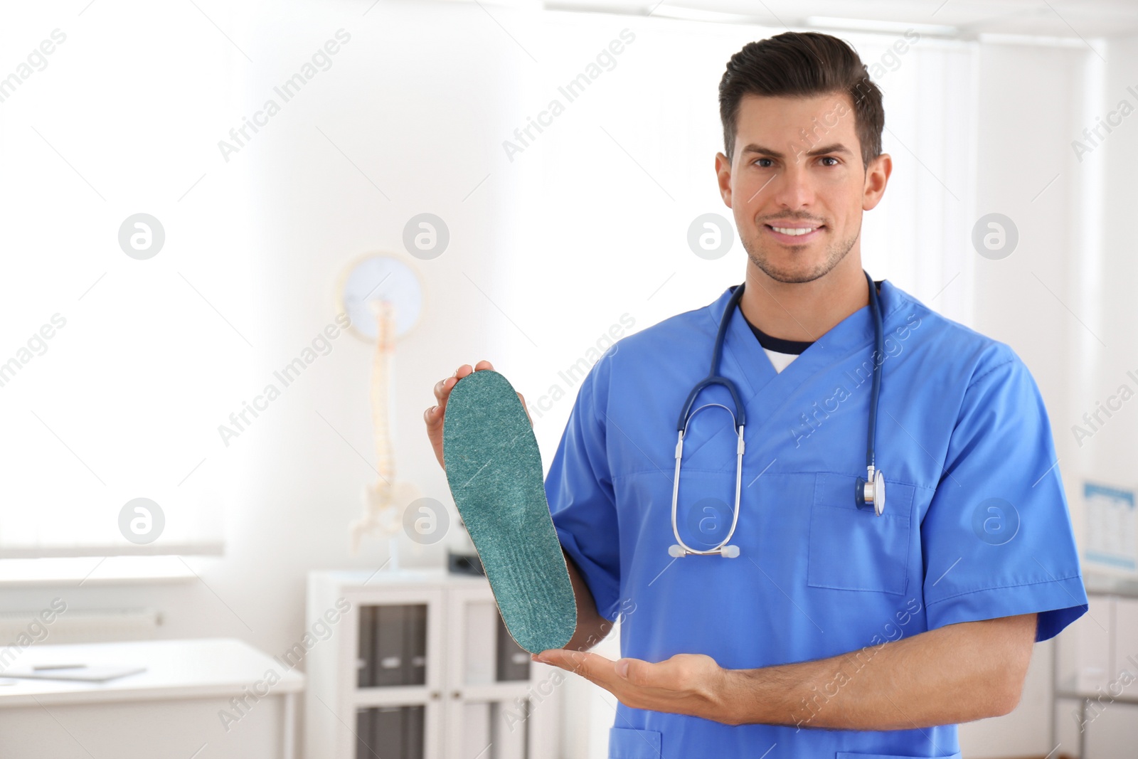 Photo of Handsome male orthopedist showing insole in clinic