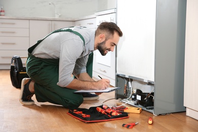 Male technician with clipboard examining refrigerator in kitchen