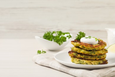 Photo of Delicious zucchini fritters with sour cream served on white wooden table, space for text