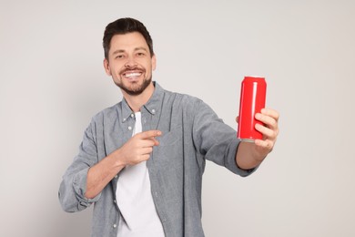 Photo of Happy man holding red tin can with beverage on light grey background