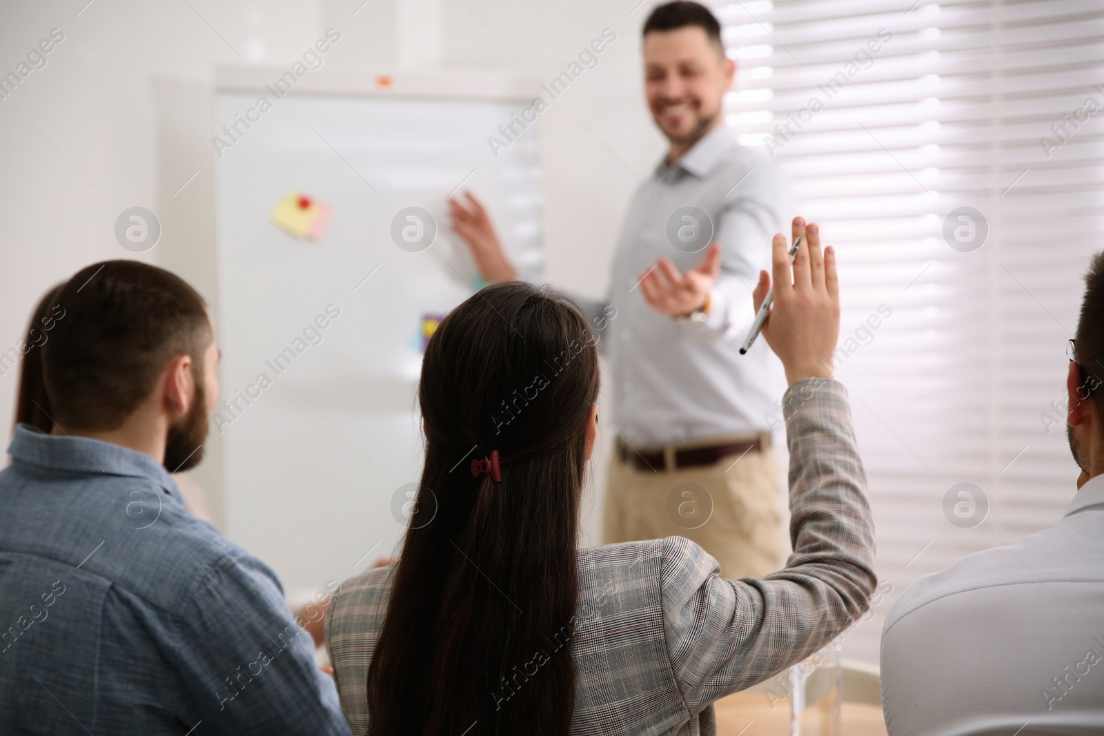 Photo of Young woman raising hand to ask question at business training in conference room