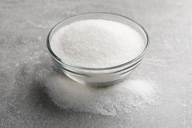 Photo of Granulated sugar and glass bowl on light grey table, closeup