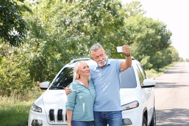 Happy senior couple taking selfie near car outdoors