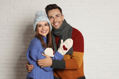 Photo of Happy young couple in warm clothes near white brick wall. Winter season