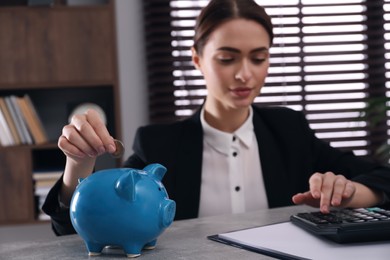 Photo of Woman putting coin into piggy bank at table in office