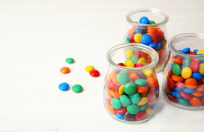 Photo of Jars with colorful candies on white wooden background. Space for text