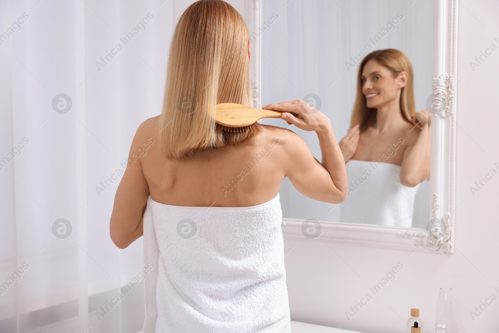 Photo of Beautiful woman brushing her hair near mirror in room