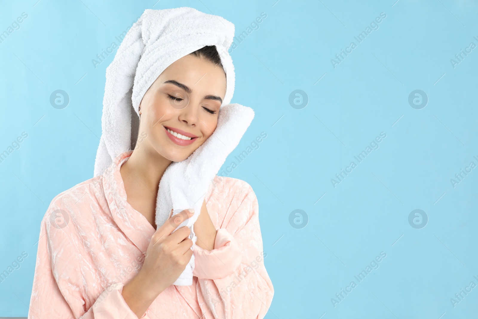 Photo of Young woman wiping face with towel on light blue background. Space for text