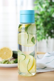 Photo of Bottle of refreshing water with cucumber, lemon and mint on wooden table indoors