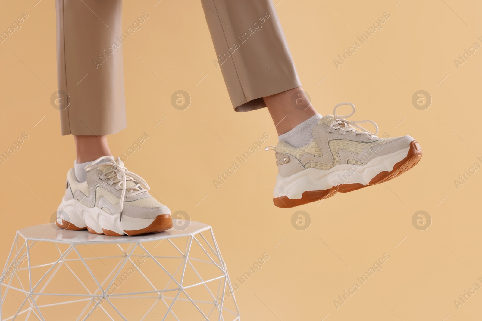Photo of Woman in stylish new sneakers standing on white table against beige background, closeup