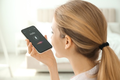 Photo of Young woman using voice search on smartphone indoors