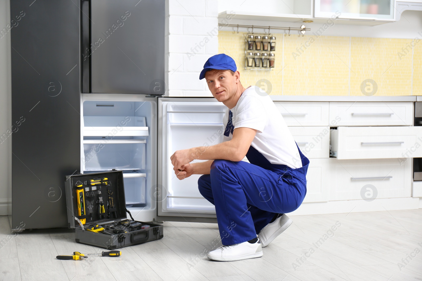 Photo of Male technician repairing broken refrigerator in kitchen