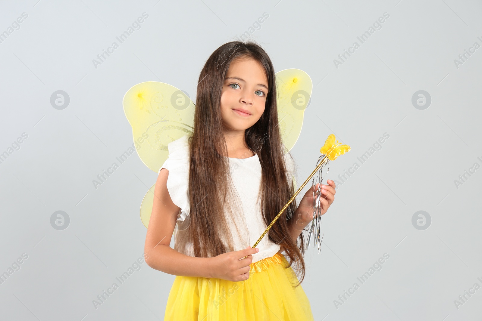 Photo of Cute little girl in fairy costume with yellow wings and magic wand on light background