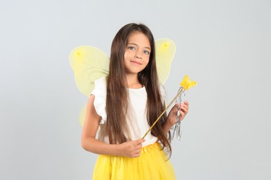 Cute little girl in fairy costume with yellow wings and magic wand on light background