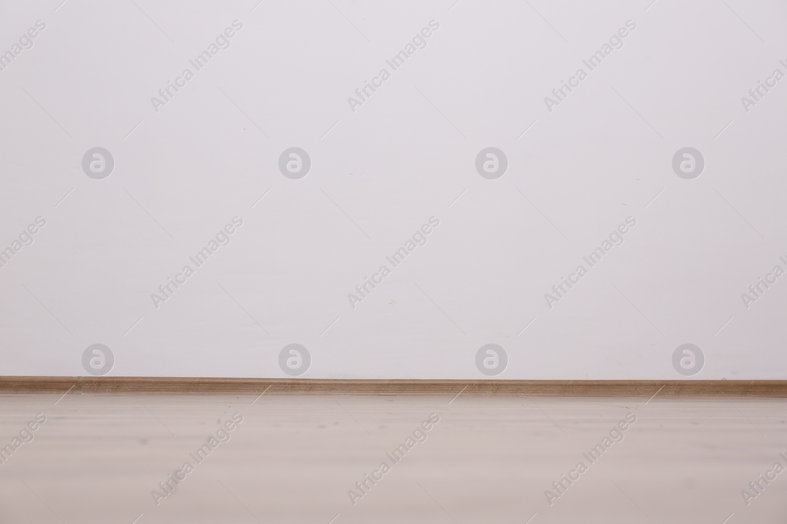 Photo of Empty white wall and wooden floor indoors, space for text