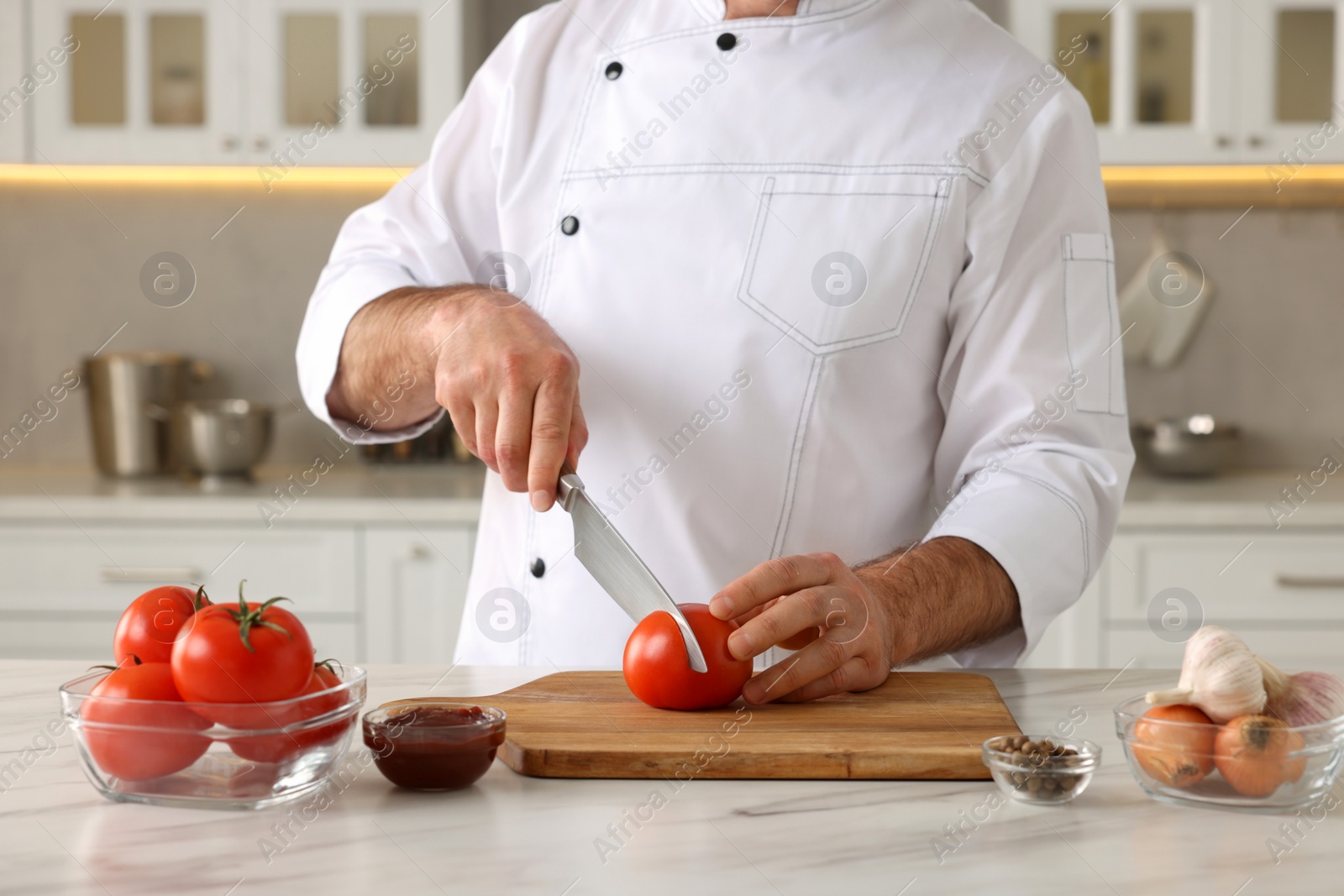 Photo of Professional chef cutting tomatoes at white marble table indoors, closeup