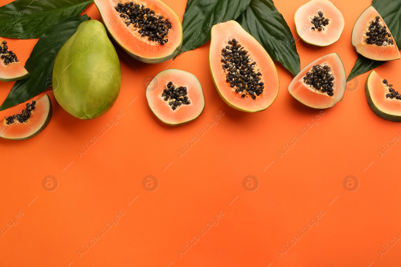 Photo of Fresh ripe papaya fruits with green leaves on orange background, flat lay. Space for text