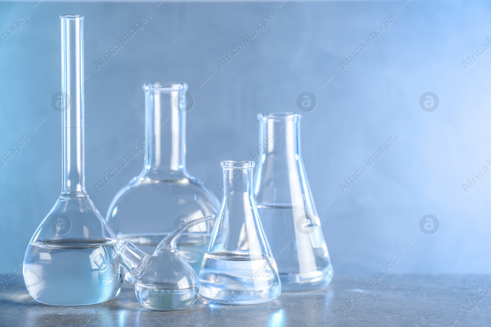 Photo of Laboratory glassware with liquid samples for analysis on grey table against toned blue background