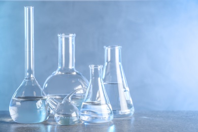 Laboratory glassware with liquid samples for analysis on grey table against toned blue background