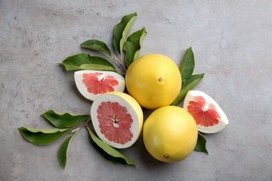 Photo of Fresh cut and whole pomelo fruits with leaves on light grey table, flat lay