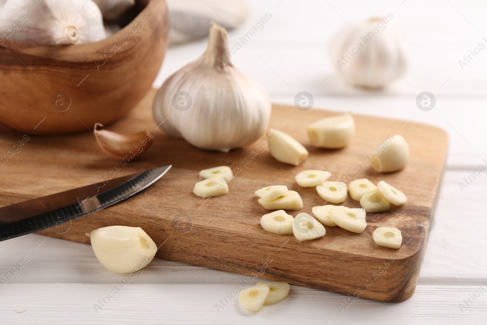 Photo of Aromatic cut garlic, cloves and bulbs on white wooden table, closeup