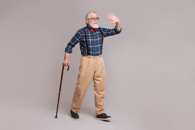 Photo of Senior man with walking cane waving on gray background