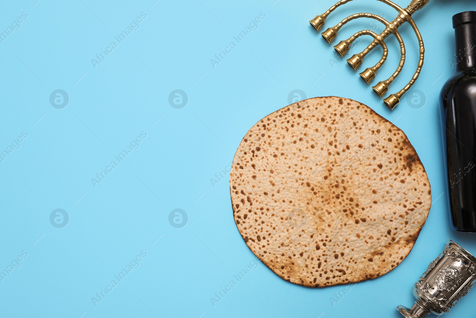 Photo of Tasty matzo, wine and menorah on light blue background, flat lay with space for text. Passover (Pesach) celebration
